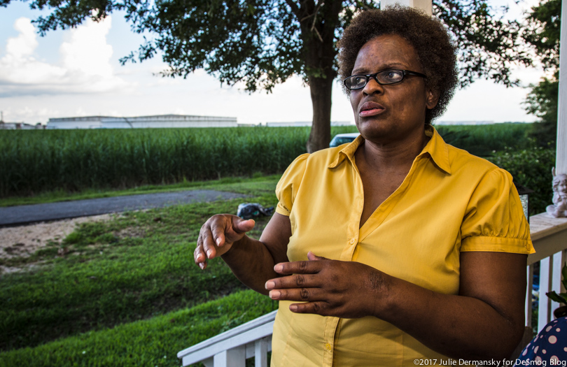 Eve Miller stands on her front porch in St. James, Louisiana, with oil tanks in the background