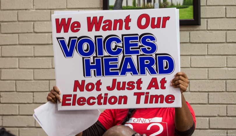 Shondrell Perrilloux holds a sign that reads 'We want our voices heard not just at election time'