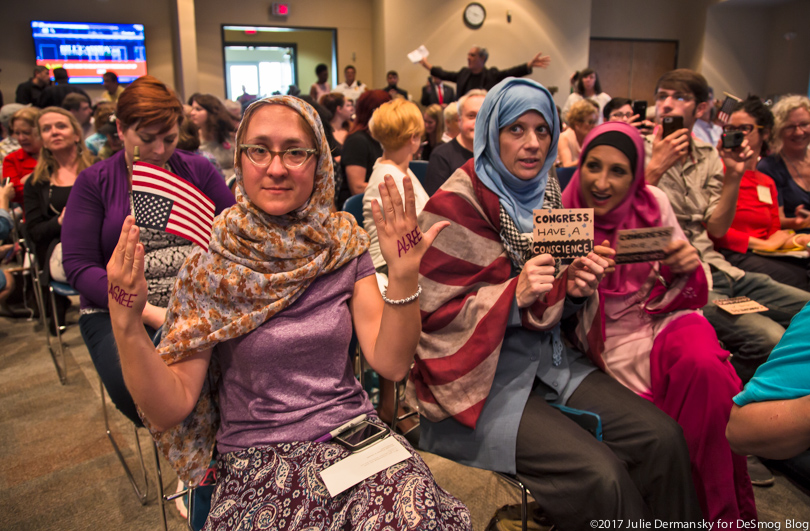 Women protest Sen. Cassidy's town hall meeting with small signs.