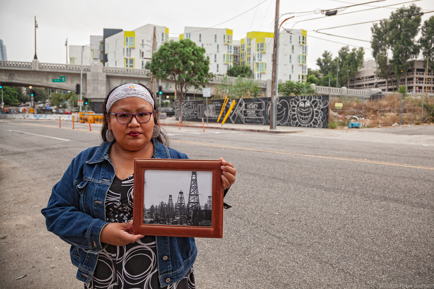Resident Esther Salas stands in front of the future site of the Echo Park Hotel, on W. 1st Street and Glendale Boulevard, a 185-room hotel. She holds a 1901 photo of the area, showing oil derricks lining the road.