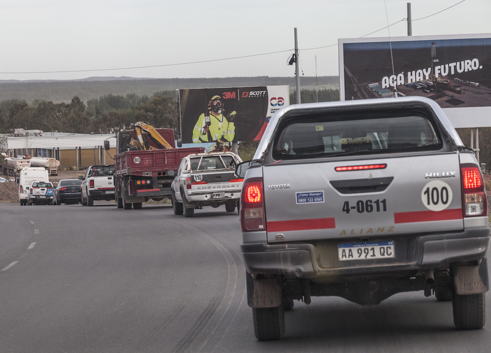 Truck traffic in Añelo, Argentina, with billboards promoting the Vaca Muerta shale