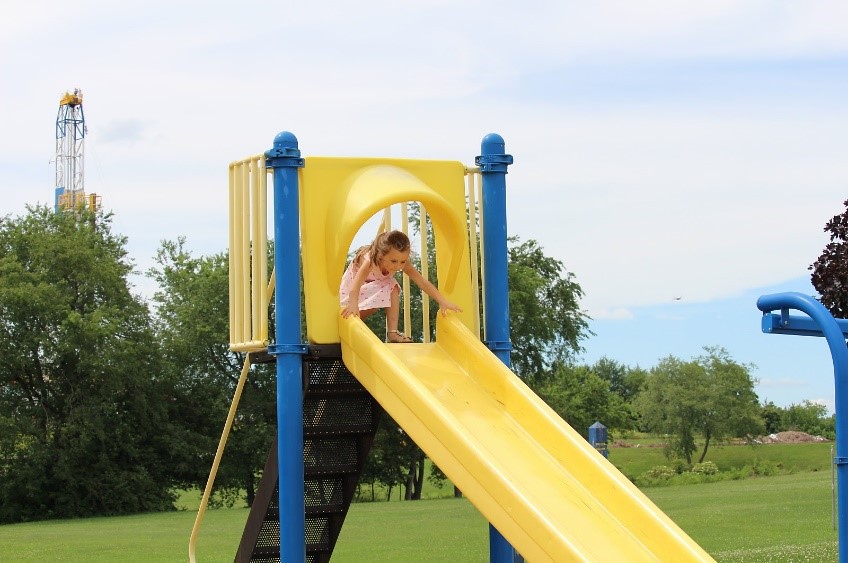 Child on a slide in a Pennsylvania playground near a drilling well pad.