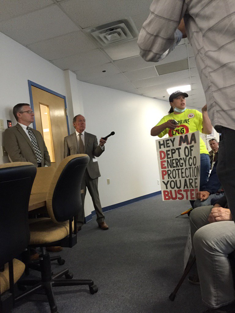 Protester holds a sign and confronts a state official over permitting practices.